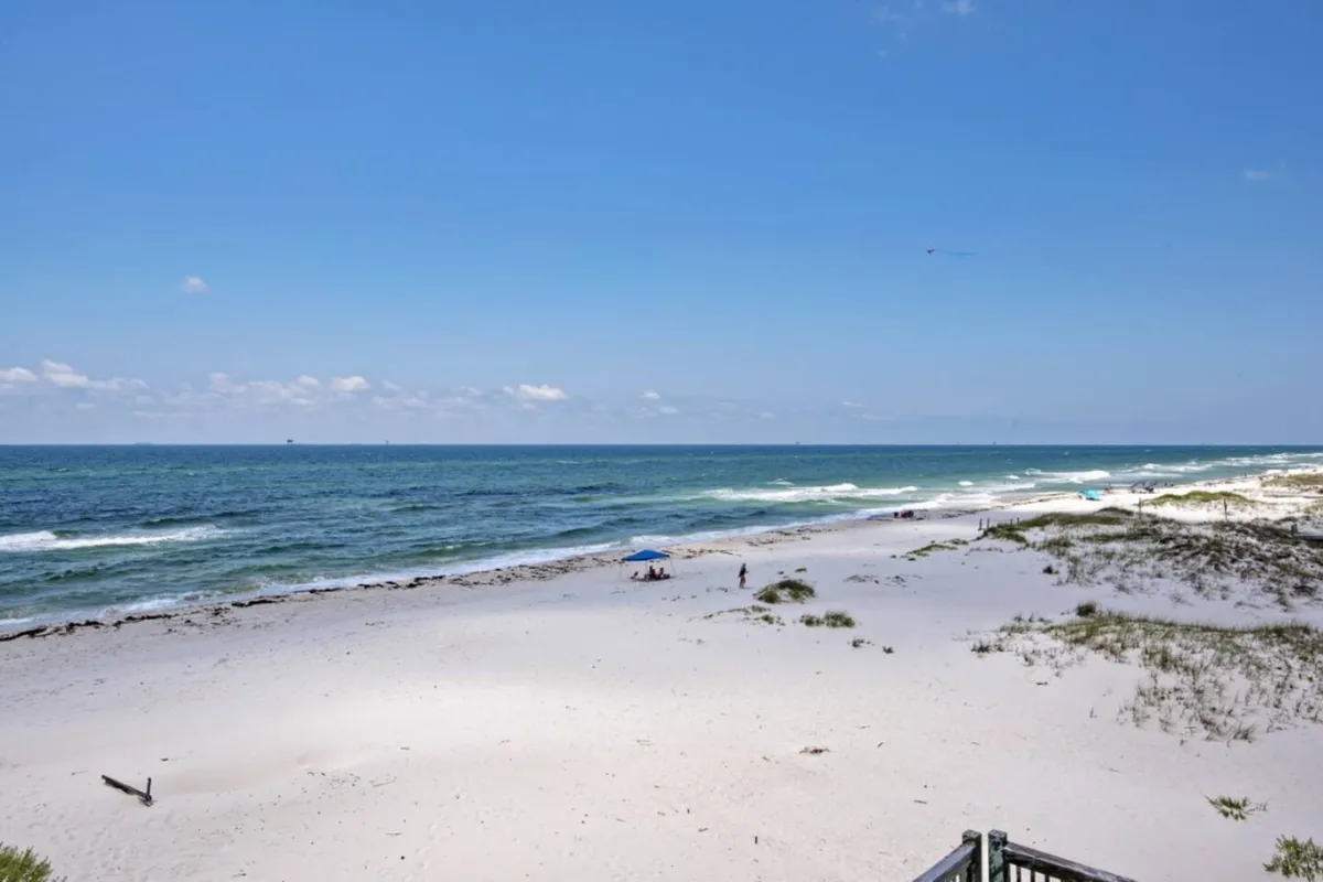A wide view of the sandy beach, ocean waves, blue sky, and umbrellas. It captures the tranquil, uncrowded stretch of shoreline and offers a sense of peace and natural beauty—perfect for sunrise walks or sunset relaxation.