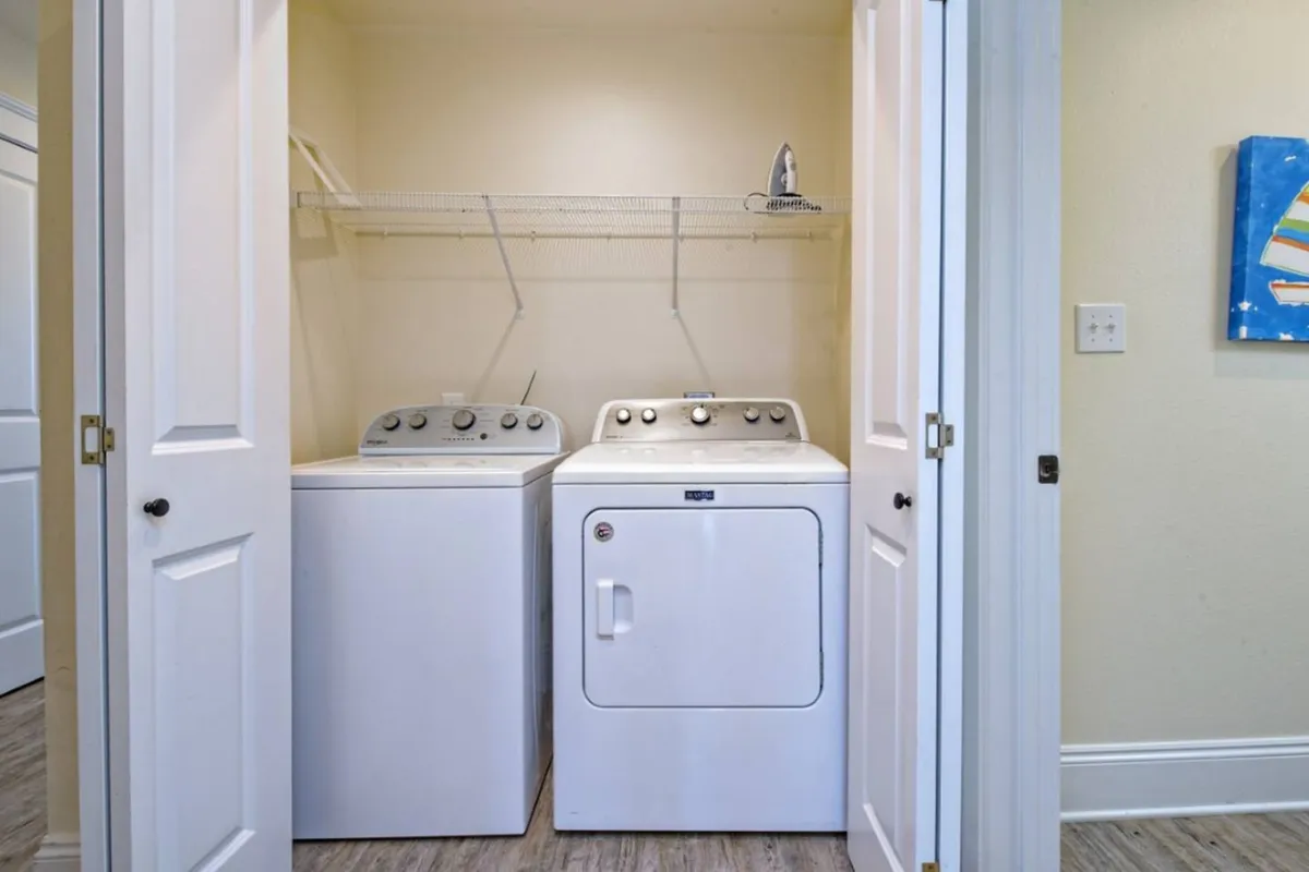A bright, organized utility room featuring a washing machine, dryer, and shelf with an iron. The space exudes a practical, tidy atmosphere ideal for handling laundry and storing household supplies.