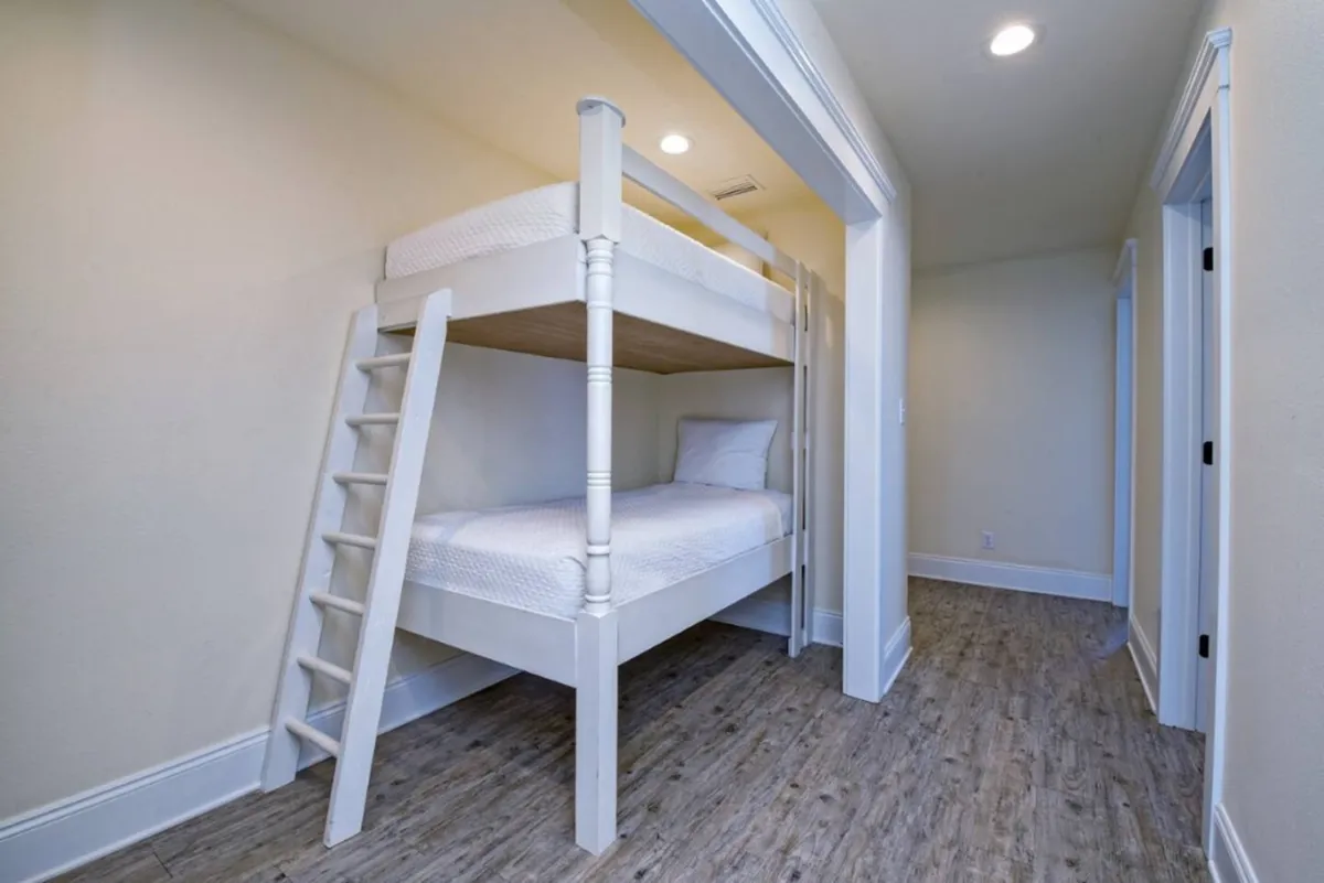 A cozy bunk room with a sturdy white bunk bed and built-in ladder. Soft bedding and a playful atmosphere make this space ideal for kids or groups, reflecting thoughtful design for comfort and togetherness.