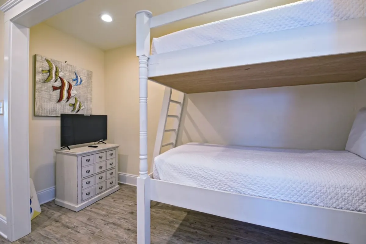 A cozy nook featuring a white wooden bunk bed with quilted bedding, a small dresser with a flat-screen TV, and colorful fish-themed wall art. The space is compact and inviting, ideal for younger guests.