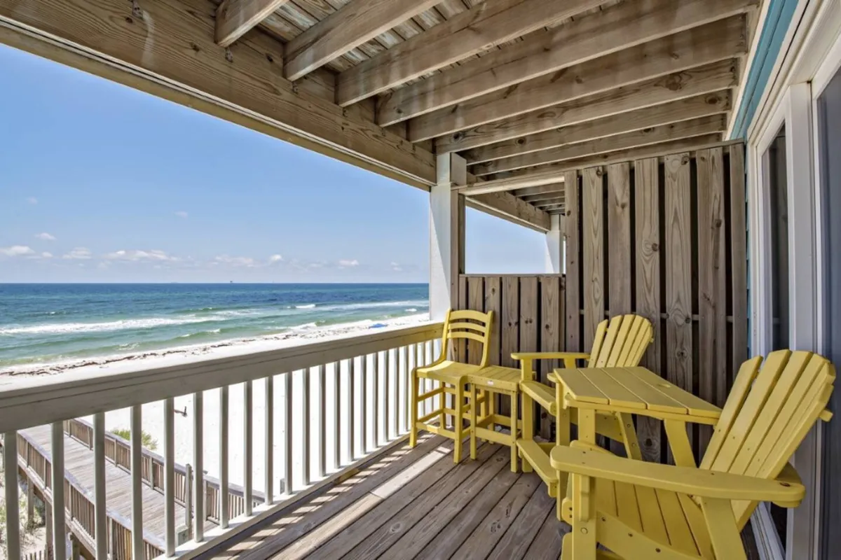 Yellow Adirondack chairs and a table set on a private wooden balcony, facing the Gulf of Mexico’s blue waters and rhythmic waves. The natural wood tones and bright, cheerful furniture invite guests to sit and unwind, with the expansive ocean view serving as a backdrop for socializing or quiet contemplation.