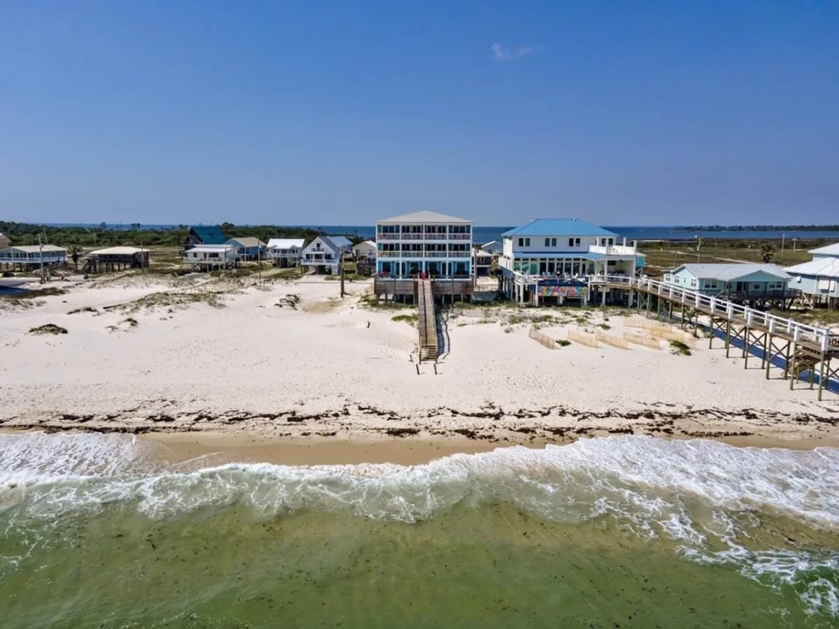 A luxurious beachfront duplex with multiple balconies, a private walkway leading directly from the house to the sugar-white sand beach, and the tranquil Gulf of Mexico waters stretching beyond. The scene exudes exclusivity, privacy, and immediate beach access, with outdoor spaces ideal for socializing or relaxing while enjoying panoramic ocean views.